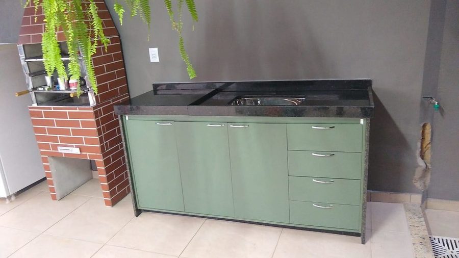 Área gourmet com bancada de granito, armário verde e churrasqueira de tijolos